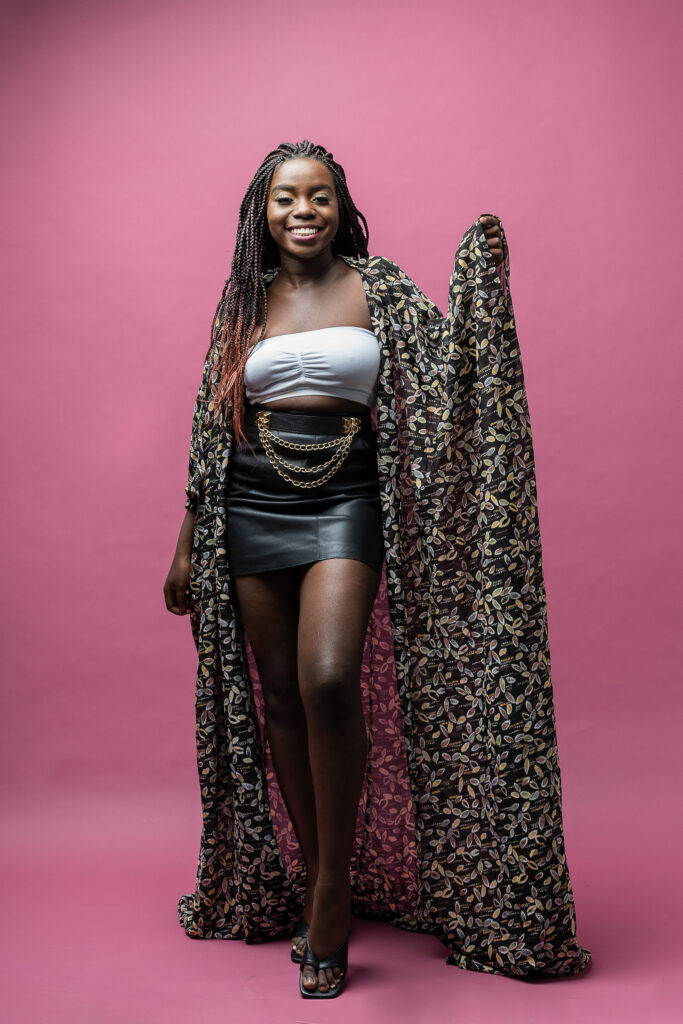 Studio fashion portrait of a woman in a silver skirt and patterned cape on a pink background