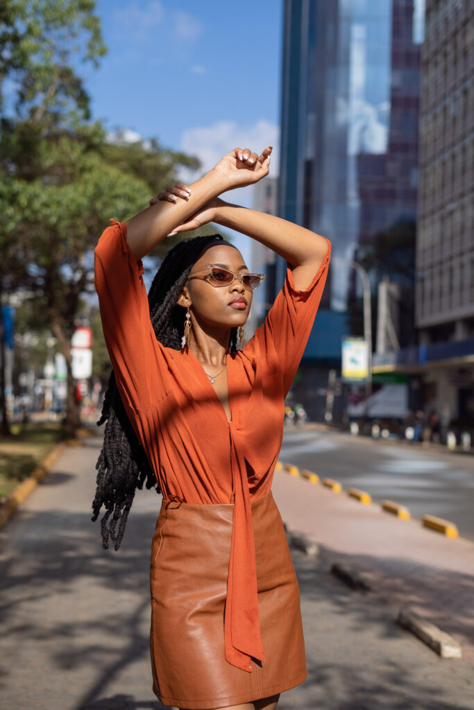 Street fashion portrait of a woman in an orange top and tan leather skirt in a city centre