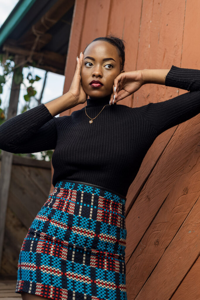 Outdoor portrait of a woman in a black top and patterned skirt beside a red timber wall