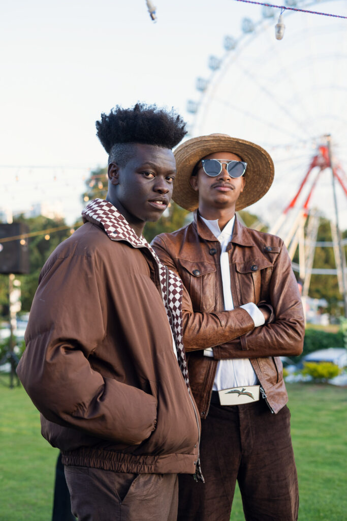 Outdoor fashion portrait of two men in brown leather jackets beside a Ferris wheel