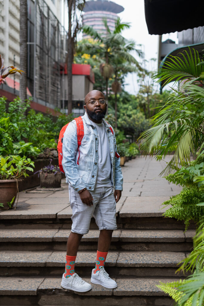 Street style portrait of a man in a denim jacket and shorts on garden steps in a city