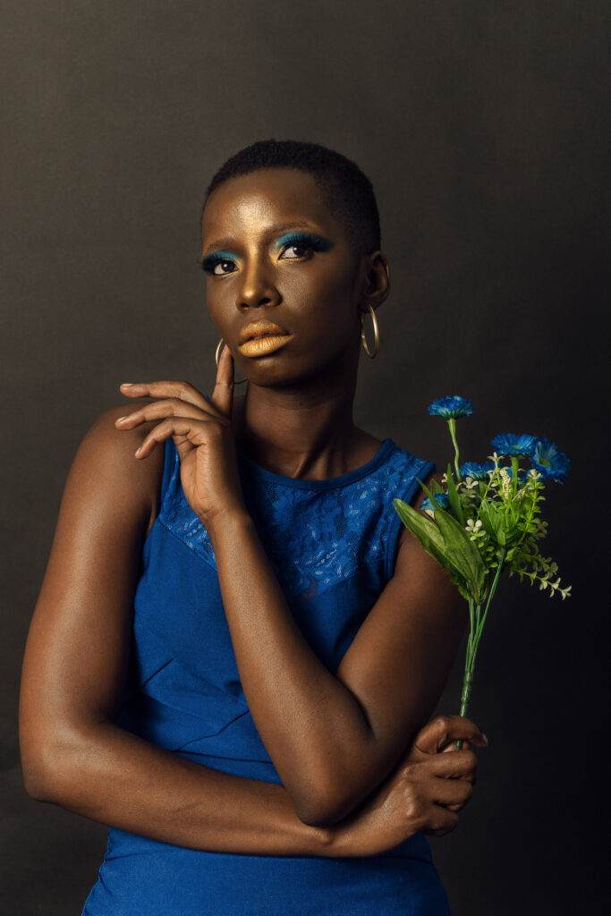 Studio portrait of a woman in a blue dress with gold eye makeup holding blue flowers