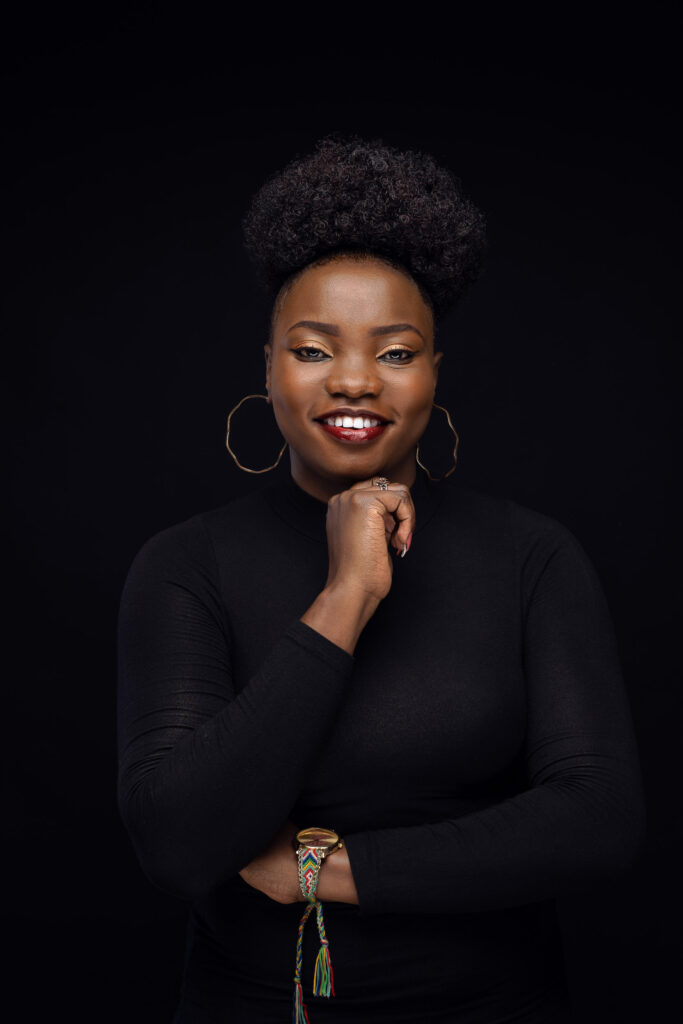 Studio portrait of a smiling woman in a black turtleneck with large hoop earrings on a black background