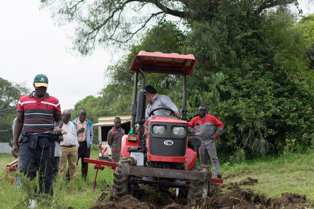 Red tractor working farmland while a group looks on