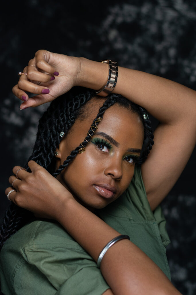 Close up portrait of a woman in a green top with braided hair and arms raised above her head