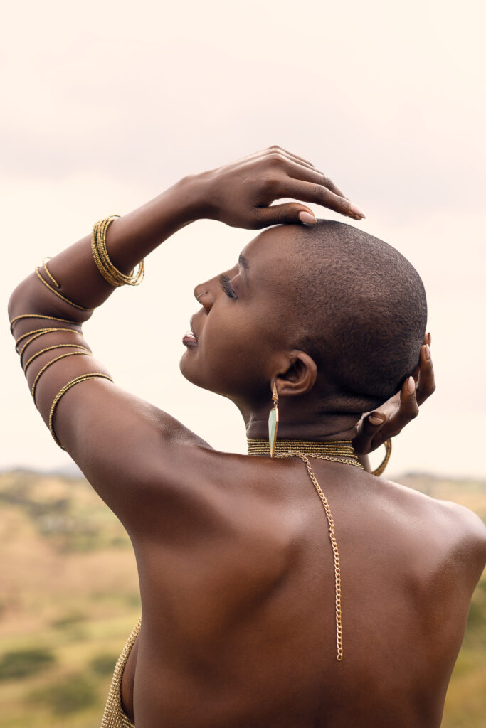 Outdoor portrait of a woman with a shaved head and gold jewellery photographed from behind