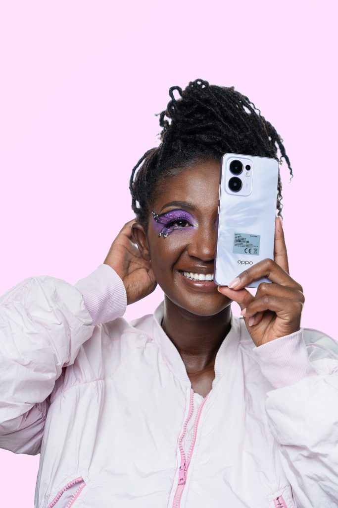 Studio portrait of a smiling woman holding a phone beside her face on a pink background